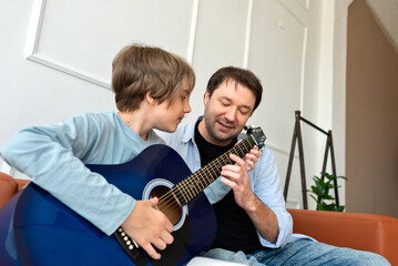 Teenager son learning to playing acoustic guitar with father support. Happy single parent family...
