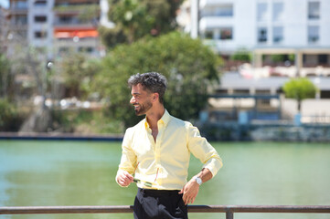 Handsome young man with beard and sunglasses in hand is leaning on the railing of the river guadalquivir in seville. On the other bank is the famous flamenco artists' quarter of Seville.