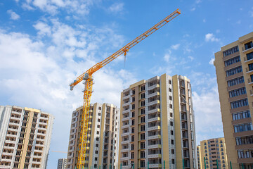 Fototapeta premium Load-lifting crane on a construction site against the blue sky. A group of lifting platforms for construction and handling operations. Close-up of a basket for transporting people