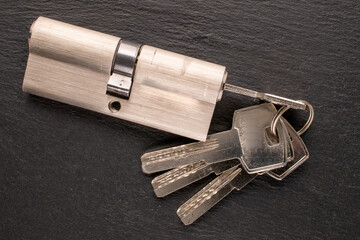 One door lock cylinder and keys on slate stone, macro, top view.