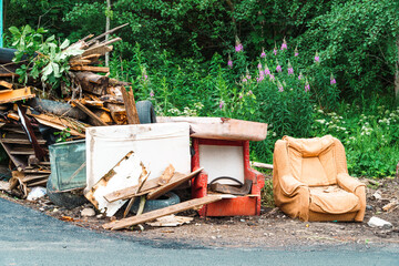 Old sofa chairs, furniture, construction garbage in the garbage dump on the grass near the forest. Concept polluting nature and city park.