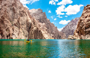 Kayaking on a mountain lake. Two men are sailing on a yellow canoe along the lake along the rocks. The theme of water sports and summer holidays. 