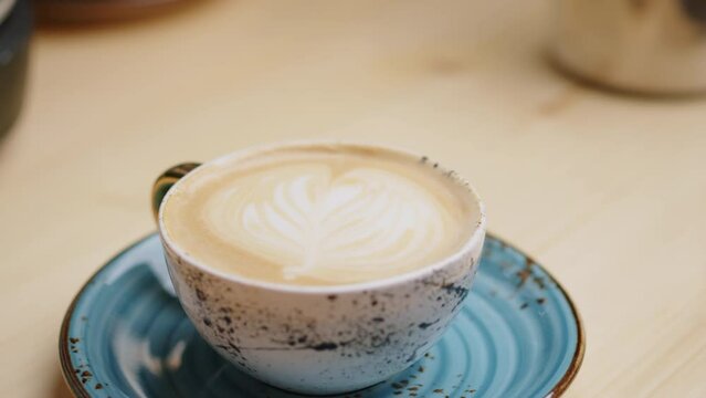 Female hand takes a beautiful handmade cup of freshly made cappuccino coffee with foam. Extreme close up macro shot