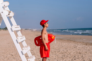 Boy lifeguard next to the watchtower on the beach