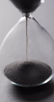 Vertical video of hourglass with sand pouring, copy space on grey background