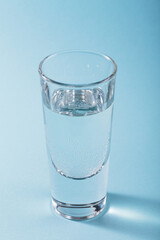 Glass of pure sparkling water on light blue background. Vertical photo with trendy shadows