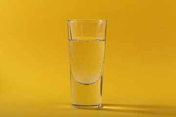 Glass of pure sparkling water on yellow background with shadow