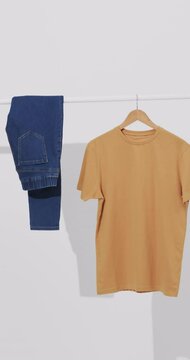 Vertical video of denim jeans and yellow t shirt on hanger and copy space on white background
