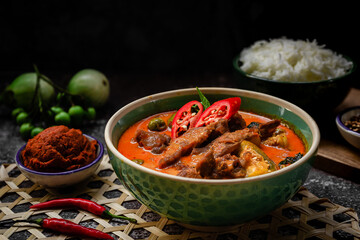 Spicy red curry on bowl and curry paste with jasmine rice on wooden cutting board rounded thai local herb - Thai food set