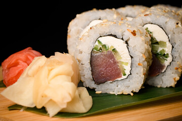 California roll with tuna, cucumber, cream cheese and sesame seeds with red and white ginger nearby served on banana leaf on wooden board