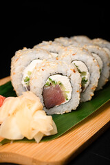 Roll with tuna, cucumber, cream cheese and sesame seeds with white ginger nearby served on banana leaf on wooden board