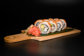 One set of California rolls covered orange tobiko with red and white ginger nearby served on banana leaves on wooden board