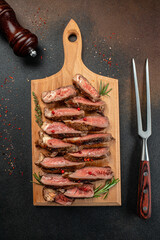 Sliced medium rare grilled steak with red wine on cutting board with rosemary and spices