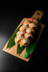 Freshly cooked California rolls covered orange masago caviar with red, white ginger and wasabi nearby served on banana leaves on wooden board
