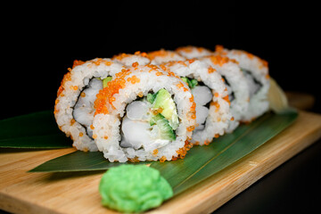 California rolls covered orange tobiko or masago caviar with served on banana leaves on wooden board on black background.