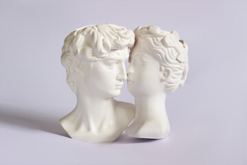 Obraz premium Two antique statue's heads isolated on a white background. Relationships of man and woman. Love, romance, kiss, tenderness. Modern design. Contemporary art. David and Aphrodite