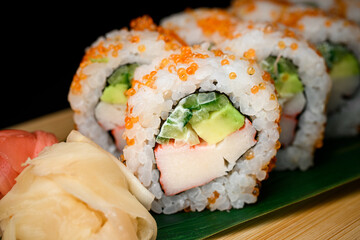 Closeup view of fresh california rolls covered with orange tobiko caviar served on banana leaves on wooden board