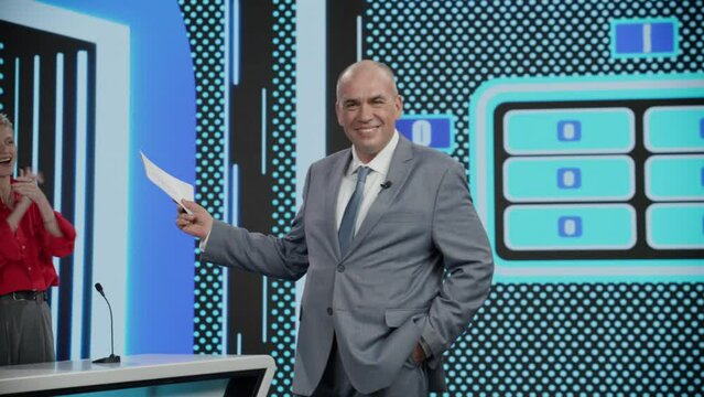 Funny charismatic host talking to the camera during recording of a fictional morning family game show