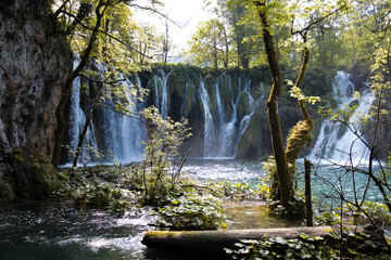 Piękny, klimatycznie oświetlony wodospad w lasku spływający do urokliwego jeziorka w Plitvickim Parku Narodowym. - obrazy, fototapety, plakaty