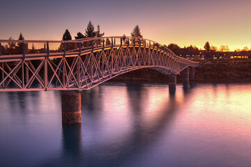 Bridge across a river at sunset. Photographed at the Maclaren footbridge across the Tekapo River, Lake Tekapo, New Zealand - obrazy, fototapety, plakaty