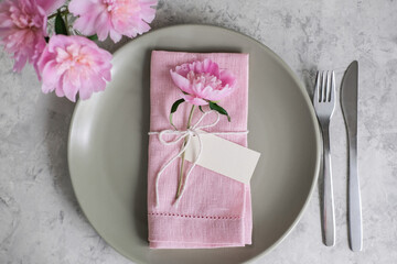 Mockup blank card for greeting or guest's name on the plate. Table setting with light green ceramic plates and pink peonies