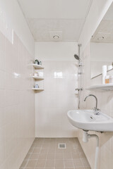 a bathroom with white tiled walls and beige tiles on the floor, there is a small sink in the corner
