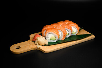 Set of Philadelphia sushi rolls on wooden board served with plant leaves, ginger and wasabi
