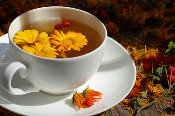 Tea with fresh calendula flowers in a white cup. There are also dried calendula flowers on the table.
