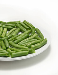 Fresh chopped green beans in a round plate, on a white background. 