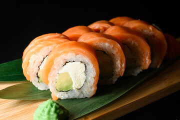 Appetizing Philadelphia sushi rolls on wooden board served with banana leaves, ginger and wasabi
