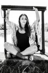 Tattooed girl, wearing a swimsuit, sitting cross-legged on a wall, black and white photo.