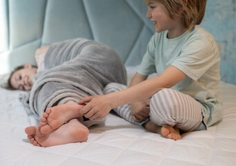 cute boy, brother tickles the bare feet of the girl, his sister wrapped in a blanket lying on the...