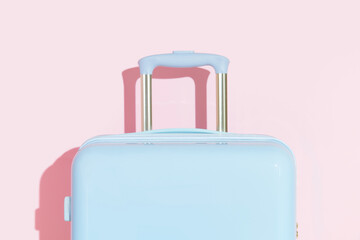 Blue suitcase on a pastel pink background with long deep shadows. Travel concept