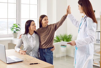 Portrait of a friendly paediatrician doctor giving high five with her little smiling girl patient standing with mother in clinic and giving the recommendations after medical examination..