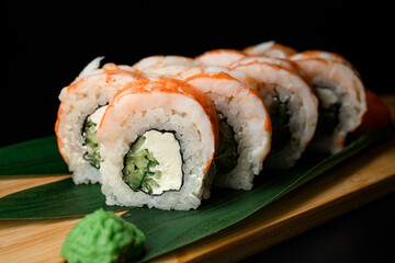 Sushi pieces with shrimp served on wooden board with plant leaves and wasabi