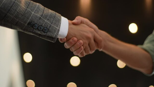 Close-up cropped shot of unrecognizable successful business people shaking hands corporate partnership deal welcoming opportunity for cooperation, on background of bokeh light.