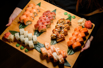 Woman holds large Philadelphia and California set Sushi Rolls with fresh fish, vegetables and cheese inside.