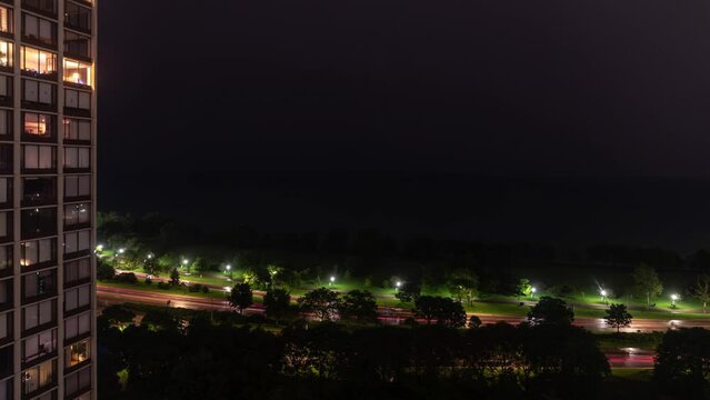 Night aerial time lapse of a storm with lightning moving over Lake Michigan at night with part of a high rise condo building to the left of frame and traffic lights on Lake Shore Drive below.