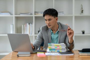 Young asian businessman working with glasses working on computer laptop in Analyze plans, search for document information, messaging keyboards, e-commerce, finance technology startup business ideas