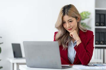 Confident Asian businesswoman While sitting at desk with laptop and doing paperwork preparing for...