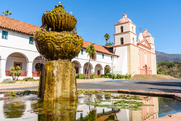 Exterior of old mission Santa Barbara on a sunny autumn morning. A fountain is in foireground. - obrazy, fototapety, plakaty