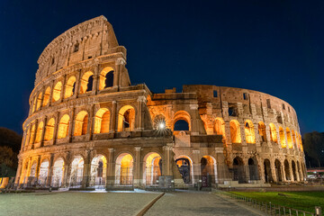Fototapeta na wymiar Nighttime photo of the Roman Colosseum. The structure is lit up with a warm orange glow set agains a cobalt blue sky. No people are visible.