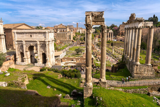 Daytime photo of three Roman ruins in the Roman Forum in Rome, Italy. Ruins of the Temple of Castor and Pollux, the Temple of Saturn, and the Arch of Septimius Severus are visible.