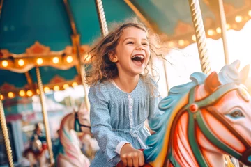 Fotobehang A happy young girl expressing excitement while on a colorful carousel, merry-go-round, having fun at an amusement park © MVProductions