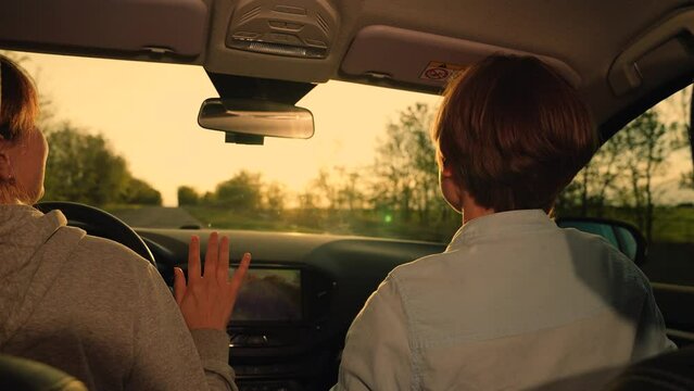 Female students driving in car listening to musical song on way sing and dance. Two happy women in car listening to radio, driving towards sun. Concept of youth, friendship, vacation travel at sunset