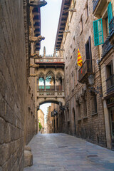 Fototapeta na wymiar Daytime photo of the Pont del Bisbe or Bishop Street Bridge, in the Gothic Quarter of Barcelona, Spain. The Catalan flag is hanging from a balcony next to turquoise window shutters.