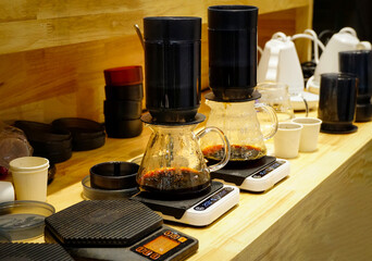 Brewing a drip hot espresso by coffee equipment such as portafilters, coffee tamper, jar, weighing machine on wooden counter, white and back tone, coffee concept.