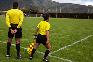 Soccer referees back to back, female assistant holds checkered flag