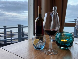 Coffee on the terrace of a restaurant with a beautiful view of the sea, with cups saucers with beverages, wine bottle, water drink and glasses on wood table looking out to ocean on light early evening
