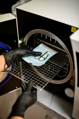 Manicurist in black gloves puts craft with manicure tools out from autoclave after sterilization
